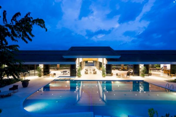 This image shows a luxurious swimming pool and a modern building at dusk, with the sky illuminated in shades of blue.