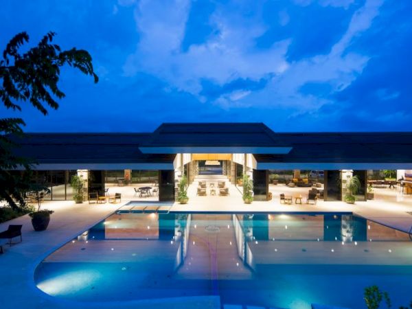 This image shows a luxurious swimming pool and a modern building at dusk, with the sky illuminated in shades of blue.