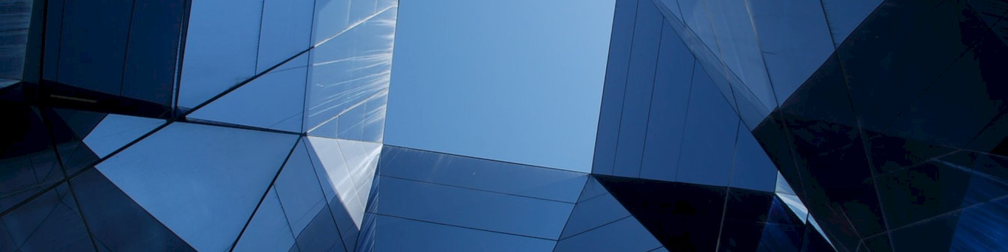The image shows a geometric pattern of reflective, modern building structures converging toward an open sky, creating an abstract architectural perspective.
