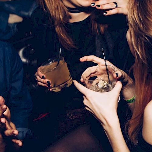 A group of people are socializing and laughing, holding drinks in their hands at what appears to be a lively gathering or party.