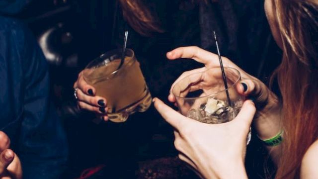 A group of people are socializing and laughing, holding drinks in their hands at what appears to be a lively gathering or party.