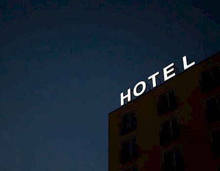 The image shows the top corner of a building with a sign that reads "HOTEL" at night against a dark sky, but the letter "E" seems to be unlit.