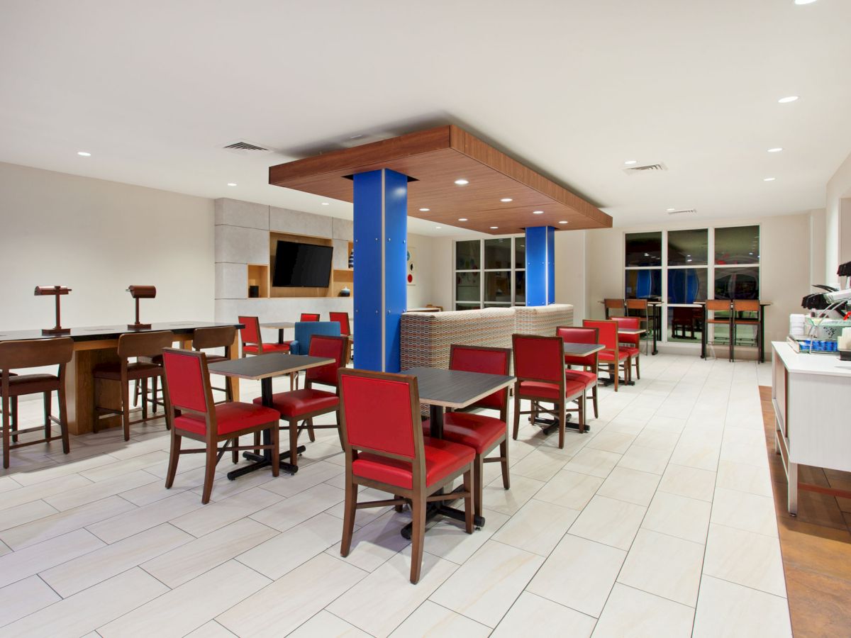 The image shows a modern, well-lit dining area with red chairs, tables, a counter, and a TV. There is a coffee machine on the right side.