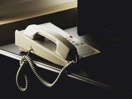 The image shows a beige landline telephone with a coiled cord placed on a desk near a window, with a dim lighting setting.