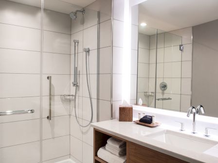 A modern bathroom with a glass-enclosed shower, a large mirror, a countertop with a sink, and neatly folded towels beneath the counter.