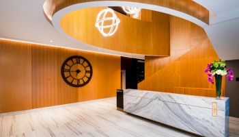 A modern lobby with wooden walls, a large clock, marble reception desk, curved architectural elements, and decorative lighting fixtures.
