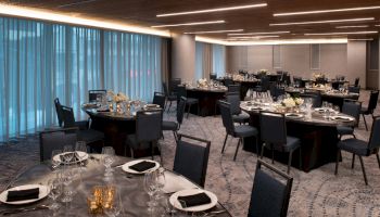The image shows an elegantly set dining area with round tables, chairs, and dim lighting, suitable for a formal event or banquet.