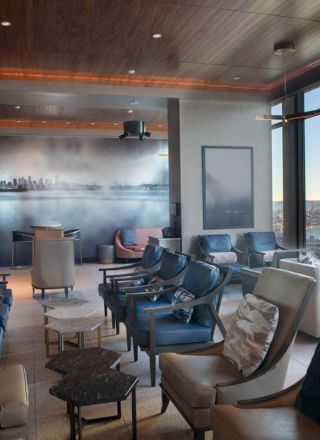 A modern lounge featuring comfortable seating, large windows with waterfront views, and a wall mural of a city skyline at dusk.