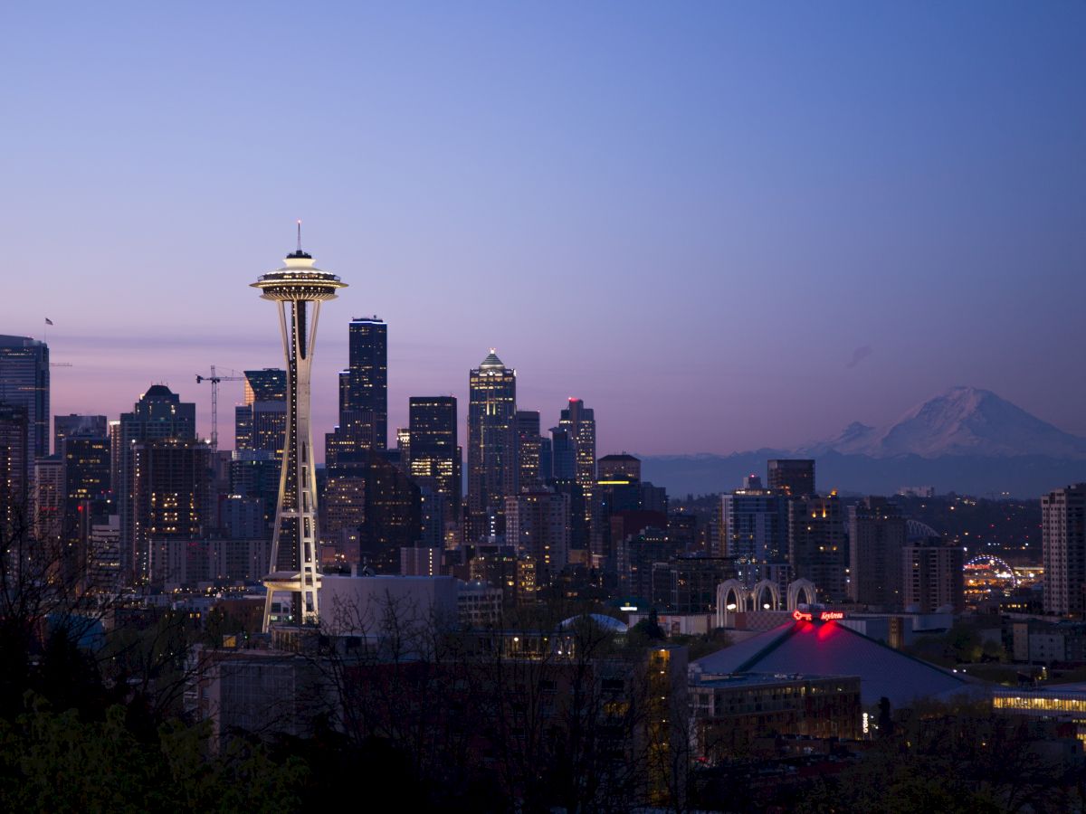 The image shows the Seattle skyline at dusk, featuring the Space Needle prominently with Mount Rainier visible in the background.